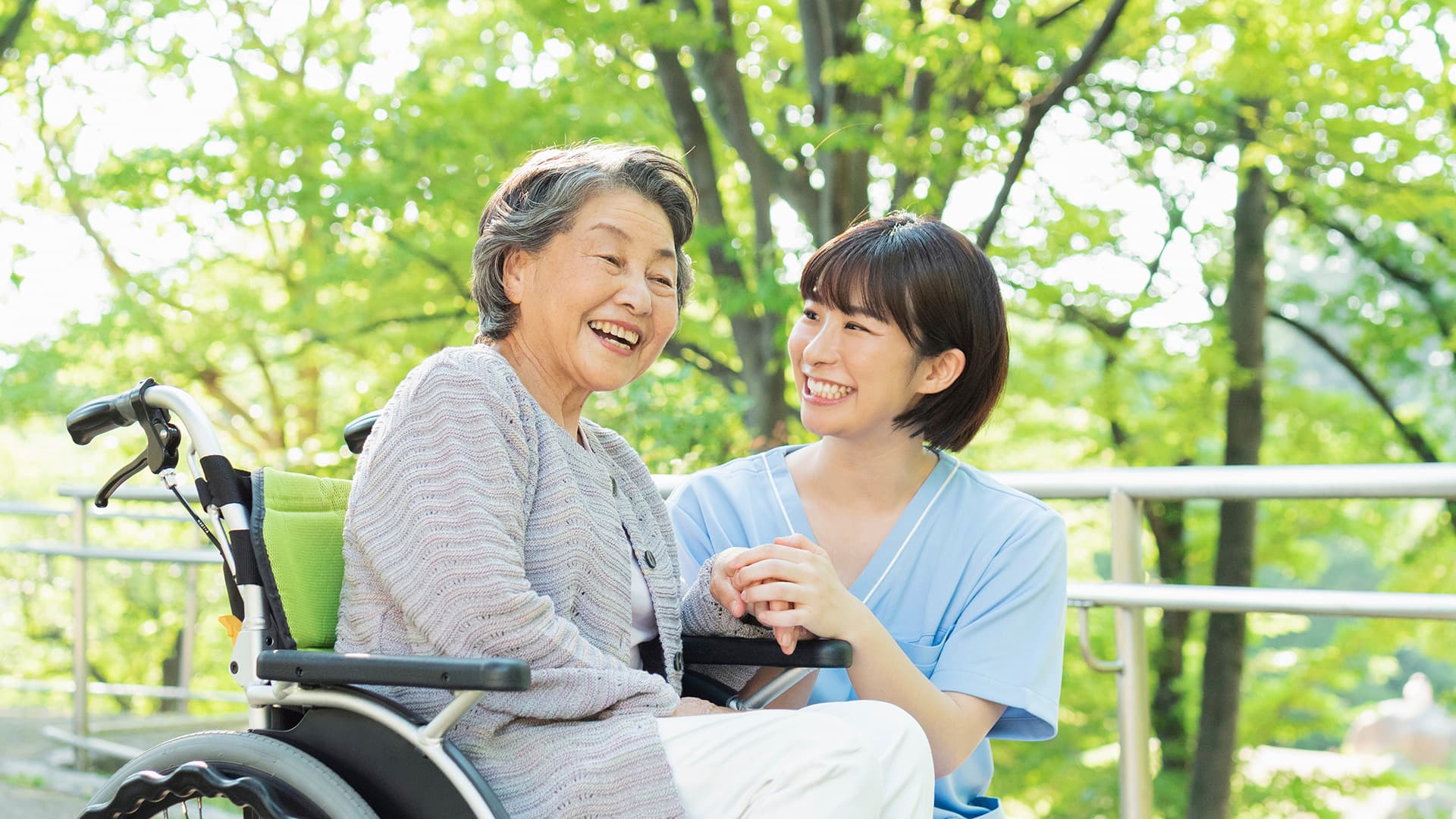 Nhân viên chăm sóc trò chuyện cùng cụ bà trên xe lăn trong khu vườn cơ sở dưỡng lão tại Nhật