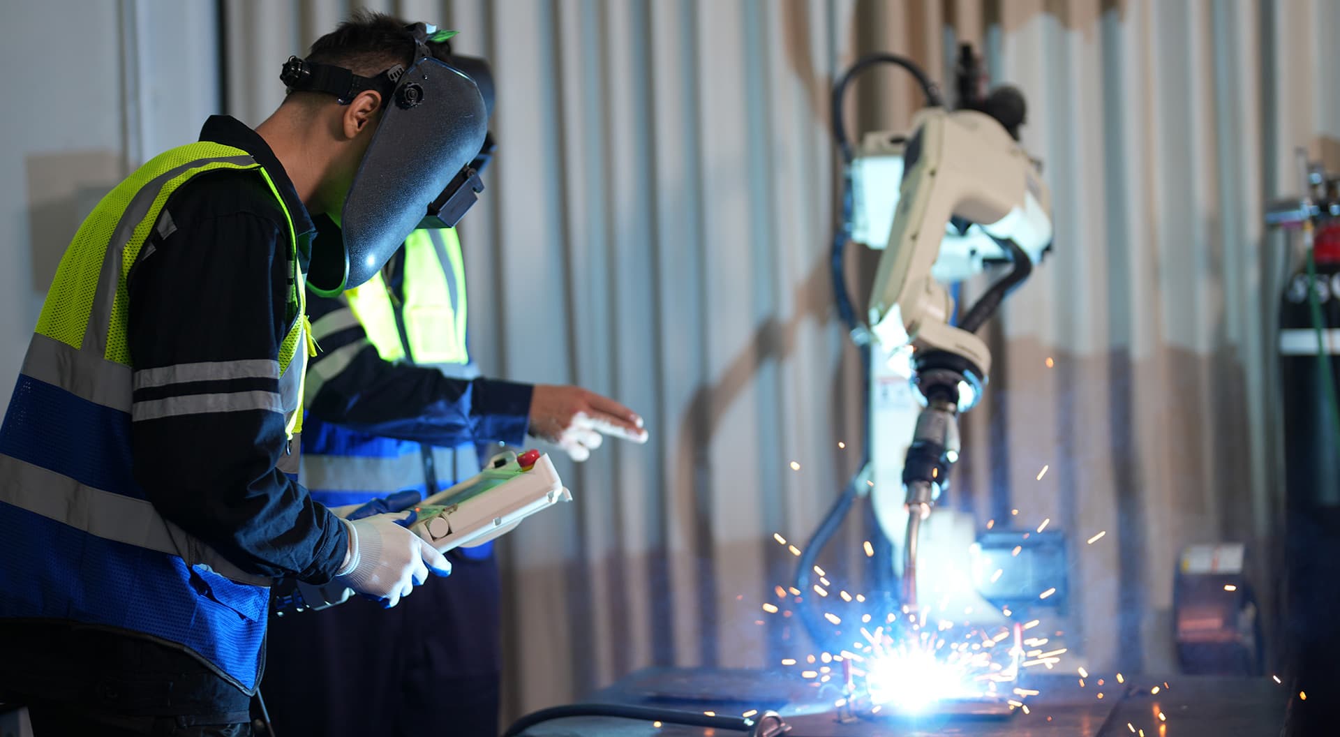 Kỹ sư trẻ lập trình robot hàn công nghiệp bằng tay điều khiển trong nhà máy Nhật