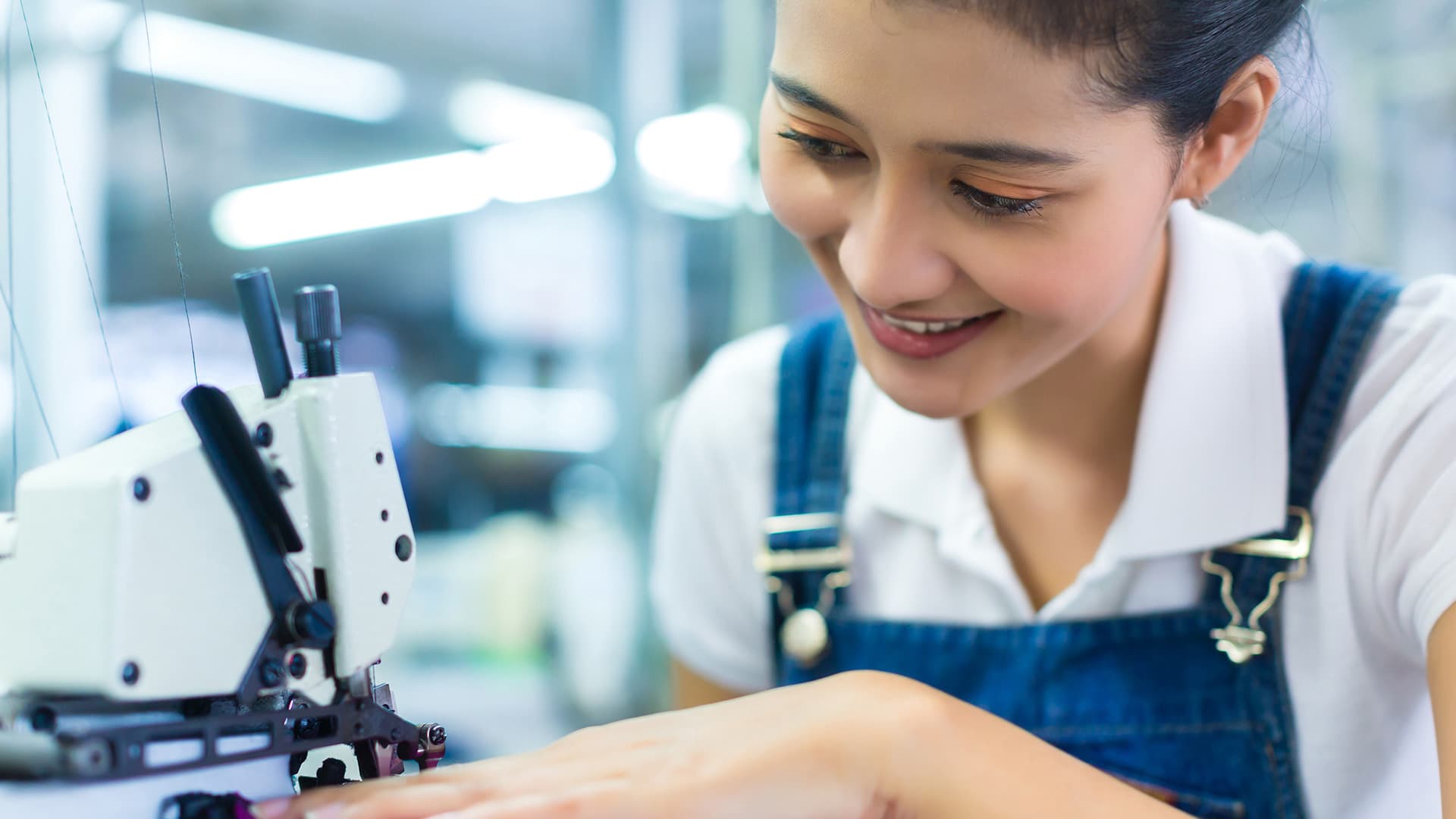Nữ công nhân may trẻ mỉm cười điều khiển máy vắt sổ trong xưởng may sáng đèn tại Nhật Bản